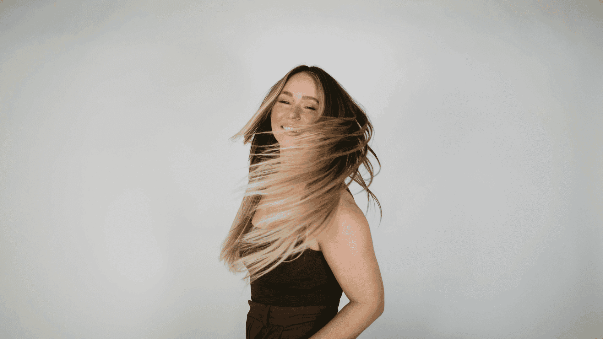 Woman smiling, flipping long hair with a blurred background.
